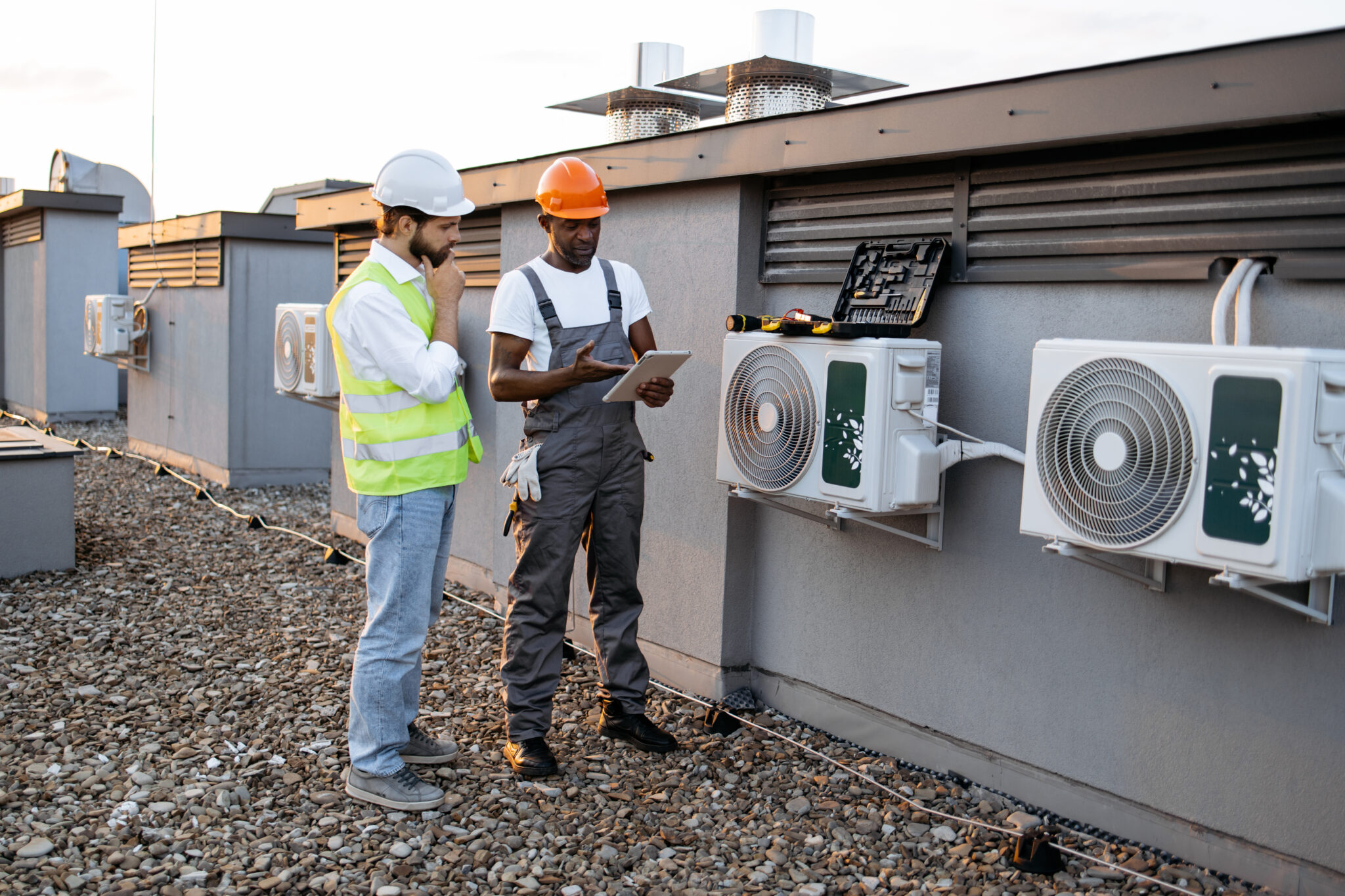 diverse workers with tablet fixing air conditioner on plant