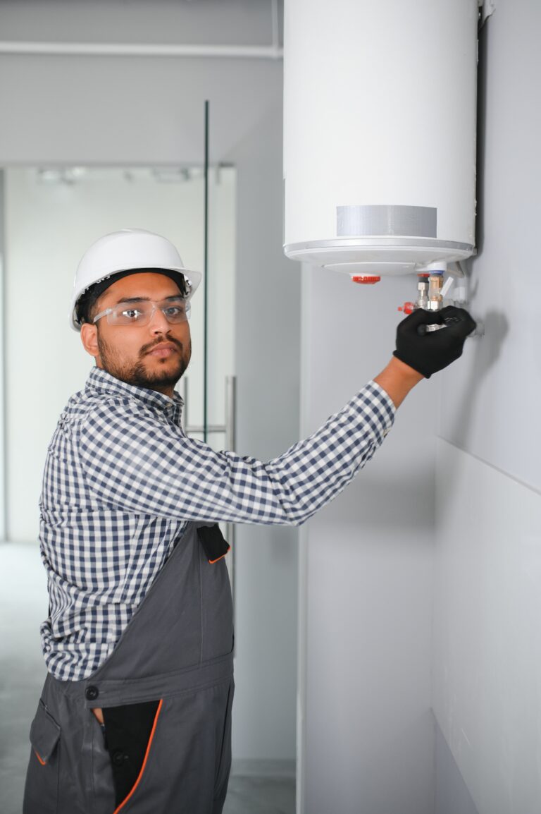 indian plumber using screwdriver while fixing boiler or water heater, working on heating system in apartment