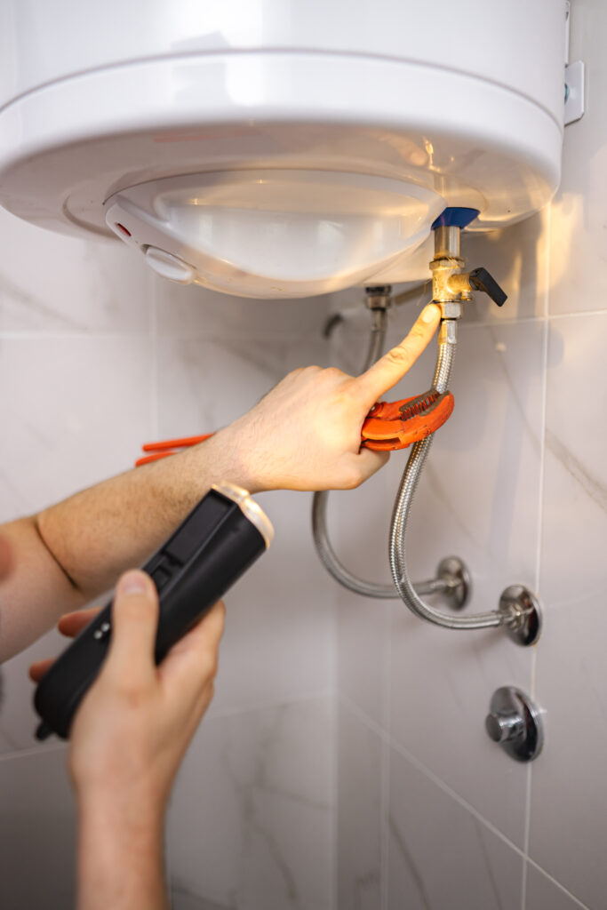 plumber working with a flashlight and pliers is fixing a water heater